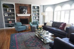 Living room , blue chairs, leather chair, fabric couch, fireplace with white mantel, bookshelves with room decor, glass coffee table, blue and red/pink area rug