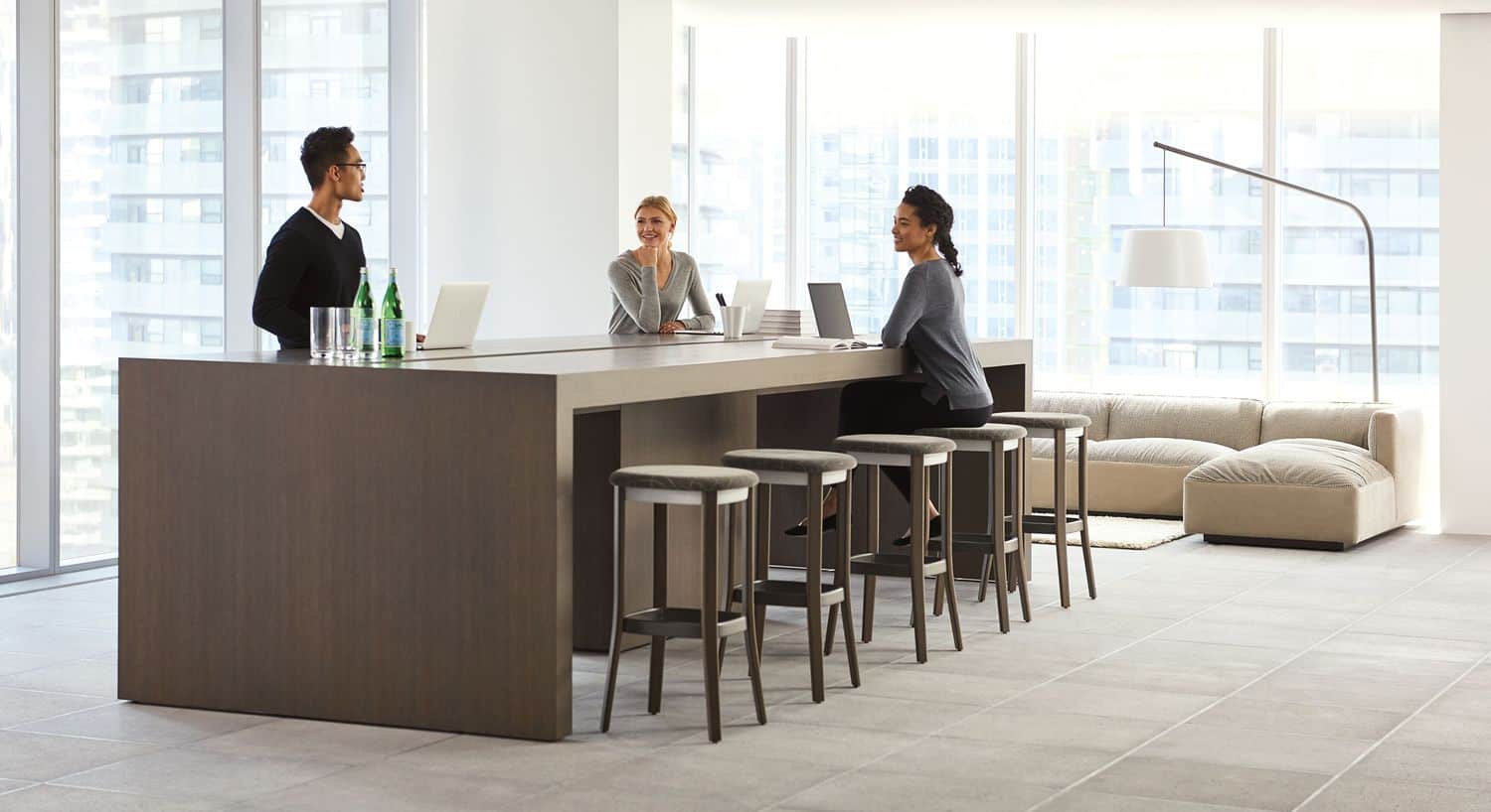 Three people standing/sitting at low community/conference table with bar stool style chairs in office